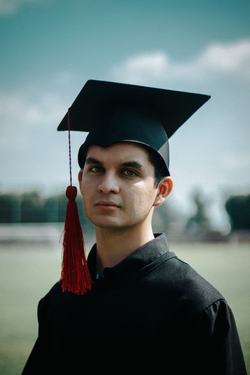 Young graduate wearing cap and gown outdoors at graduation